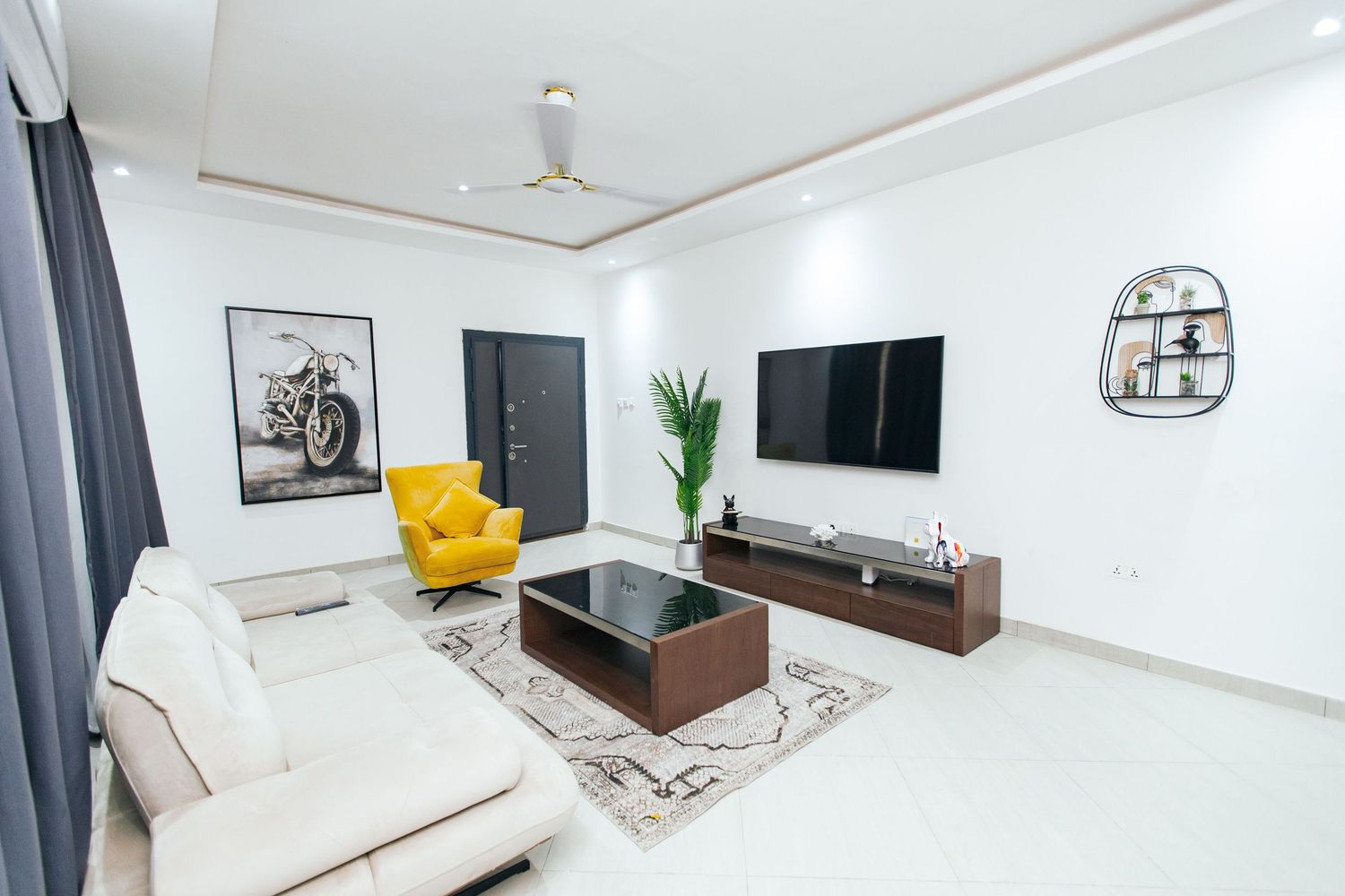 Bright living room featuring white walls, wooden furniture, and stylish yellow accent pieces.