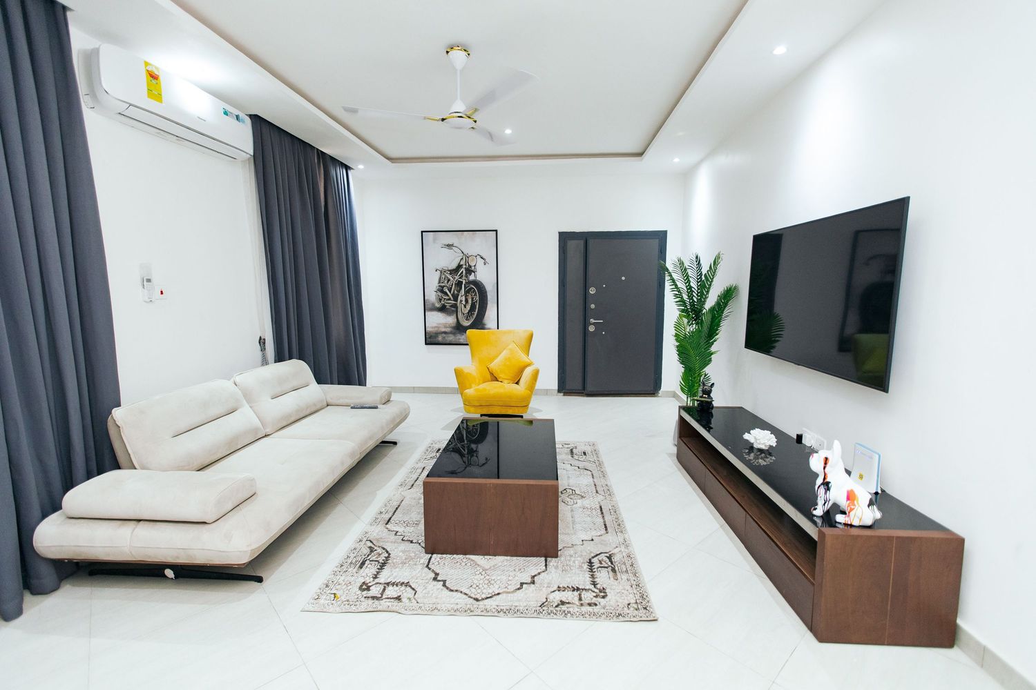 Modern living room with white walls, dark curtains, mounted TV, and beige sofa on a patterned area rug.