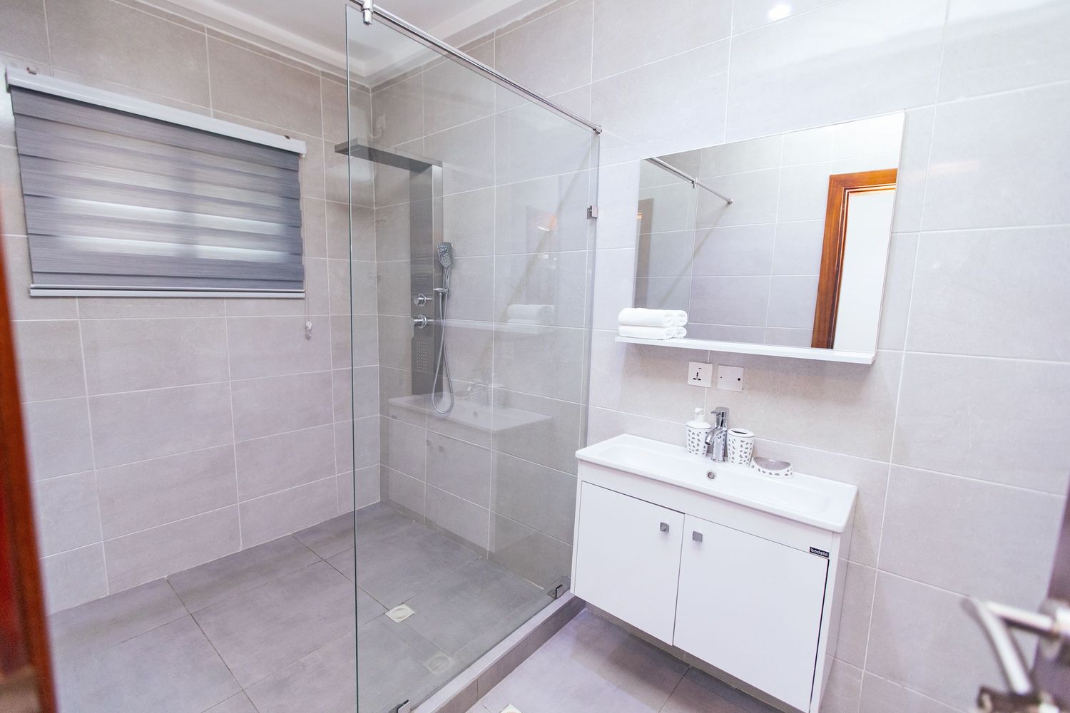 Sleek bathroom featuring white tiles, glass shower partition, and floating vanity cabinet.