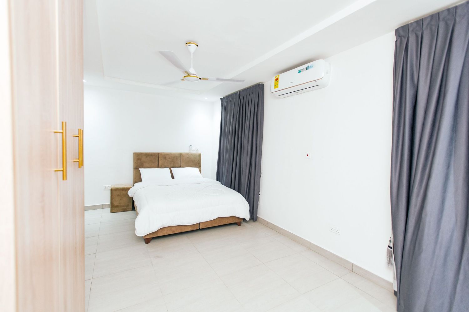 Clean white bedroom interior with ceiling fan, wooden furniture, and gray drapes creating a serene atmosphere.