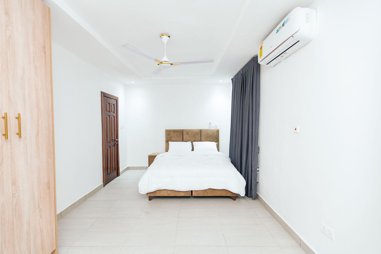 Modern minimalist bedroom with white walls, wooden accents, and gray curtains features a comfortable bed and air conditioning.