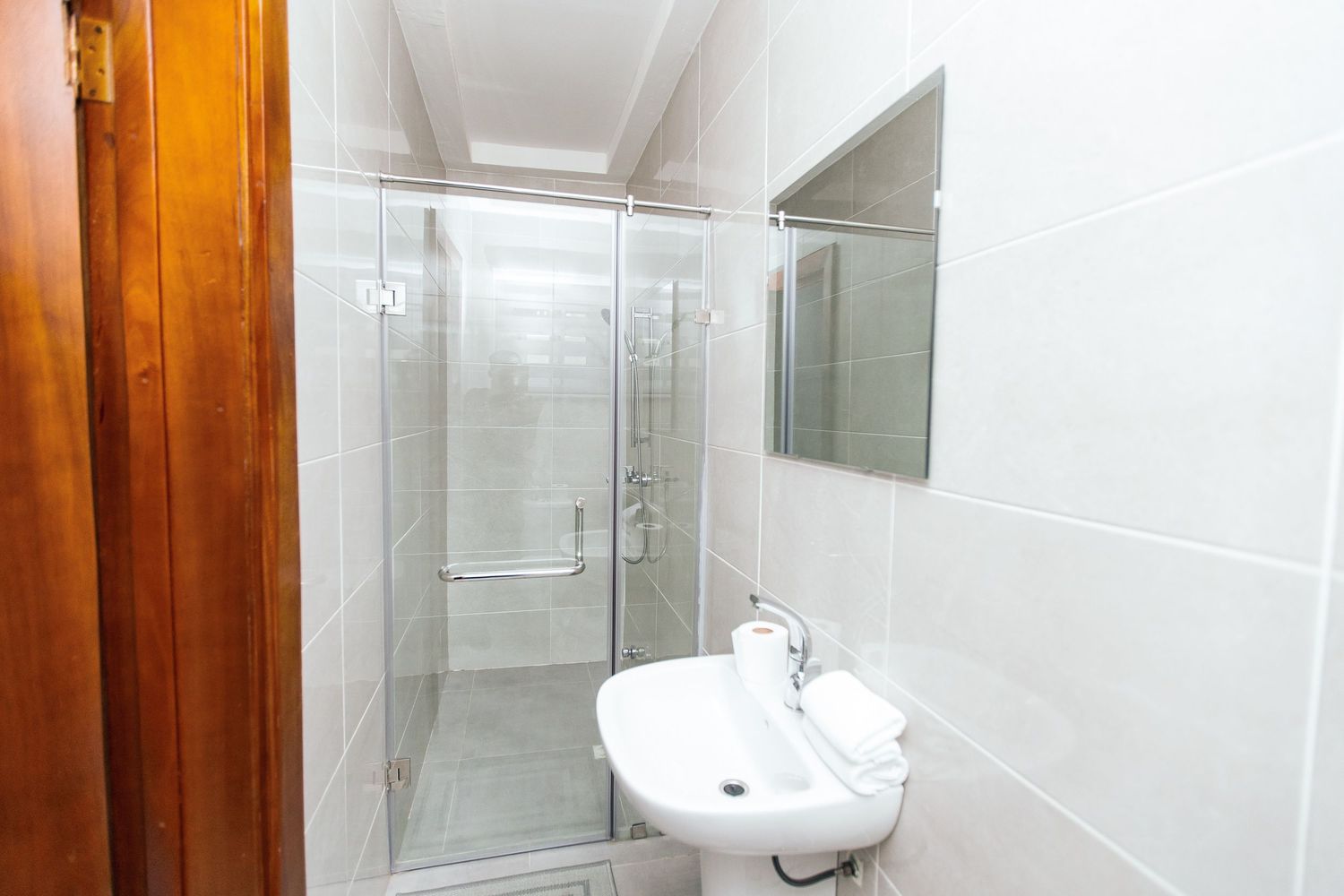 Bright white bathroom interior featuring glass shower partition and modern sink with wooden door accent.