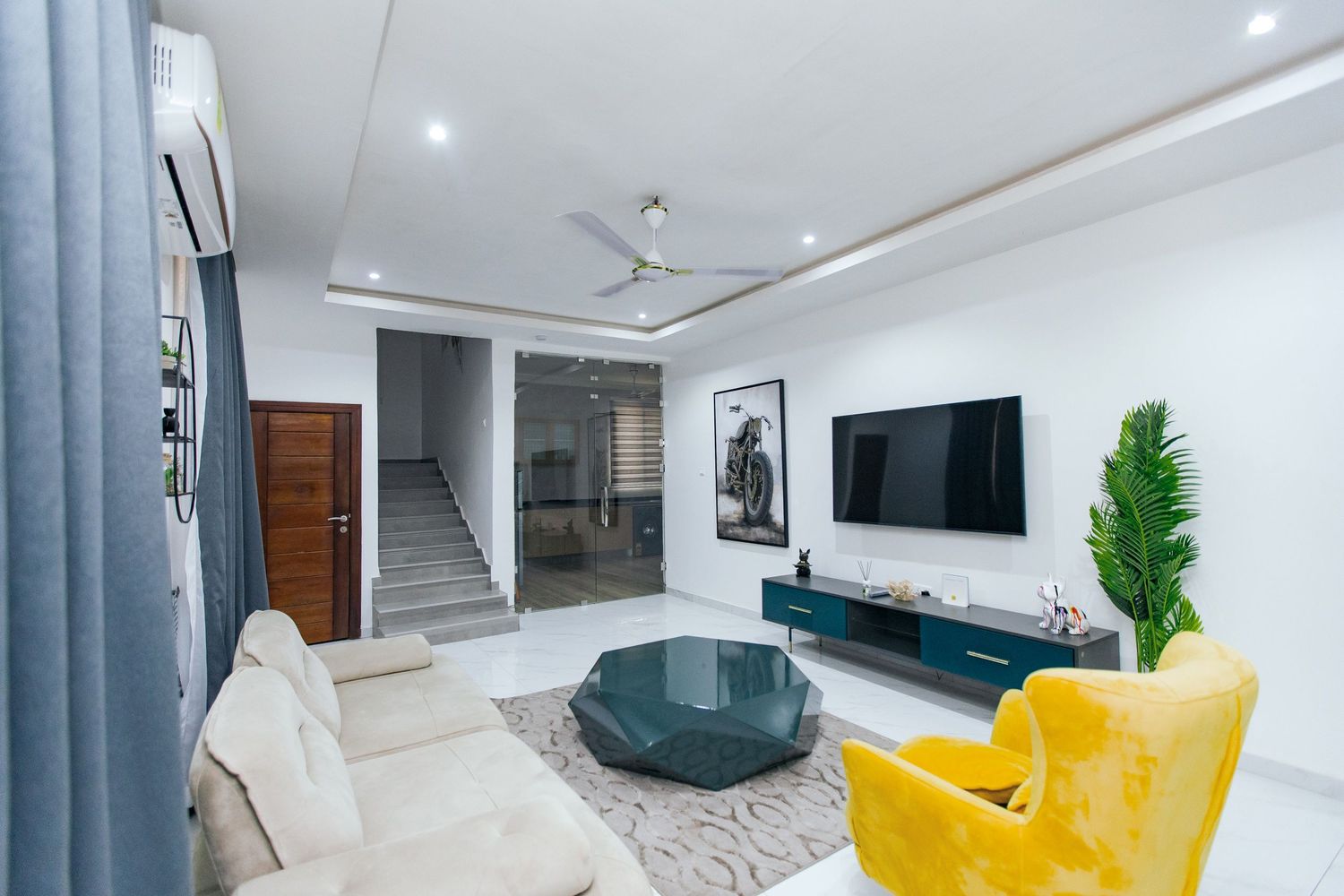 Modern living area with yellow accent chair, wall-mounted TV, and teal feature wall creating vibrant contrast.