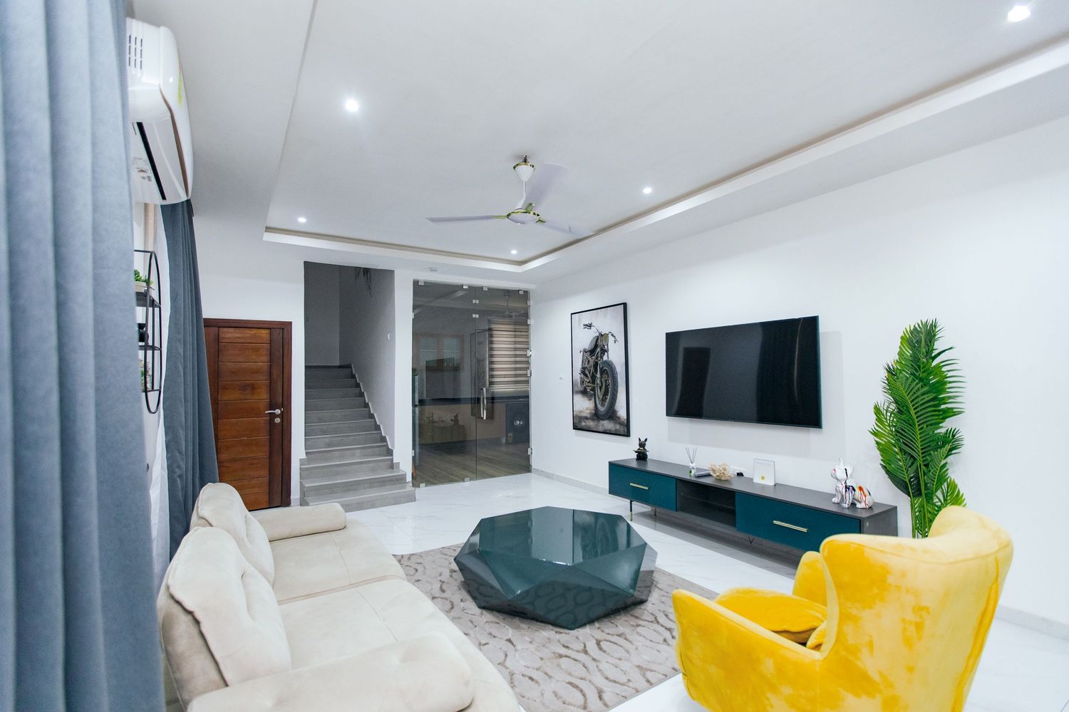 Stylish living room interior with yellow accent furniture, mounted TV, and decorative plants adding natural elements.