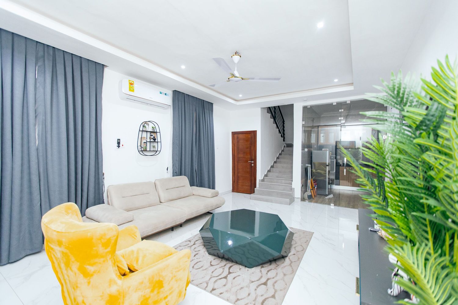 Open concept living space with yellow statement chair, teal accent wall, and modern entertainment setup.