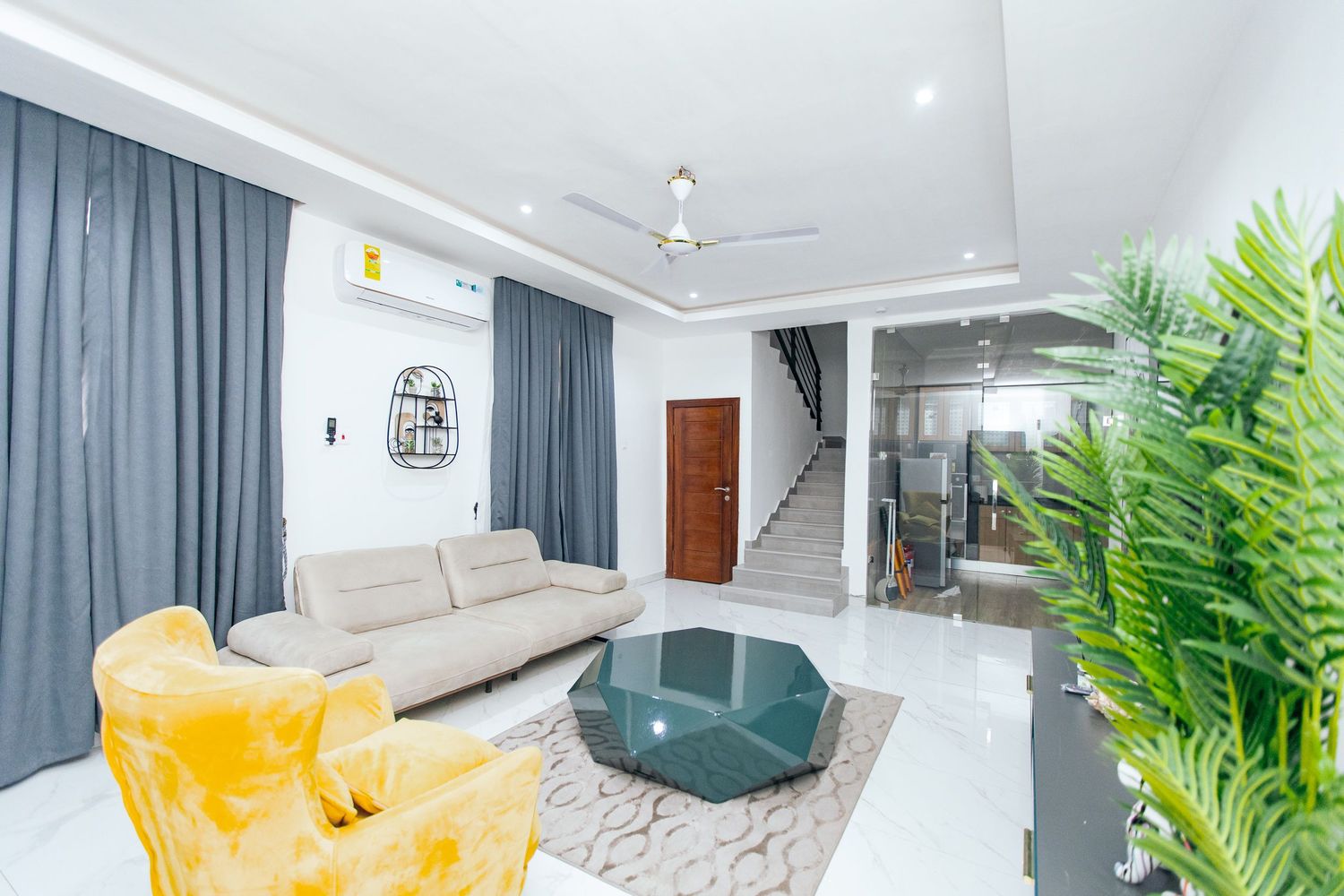 Modern living room with white walls, teal accents, yellow armchair, and contemporary decor featuring clean lines.