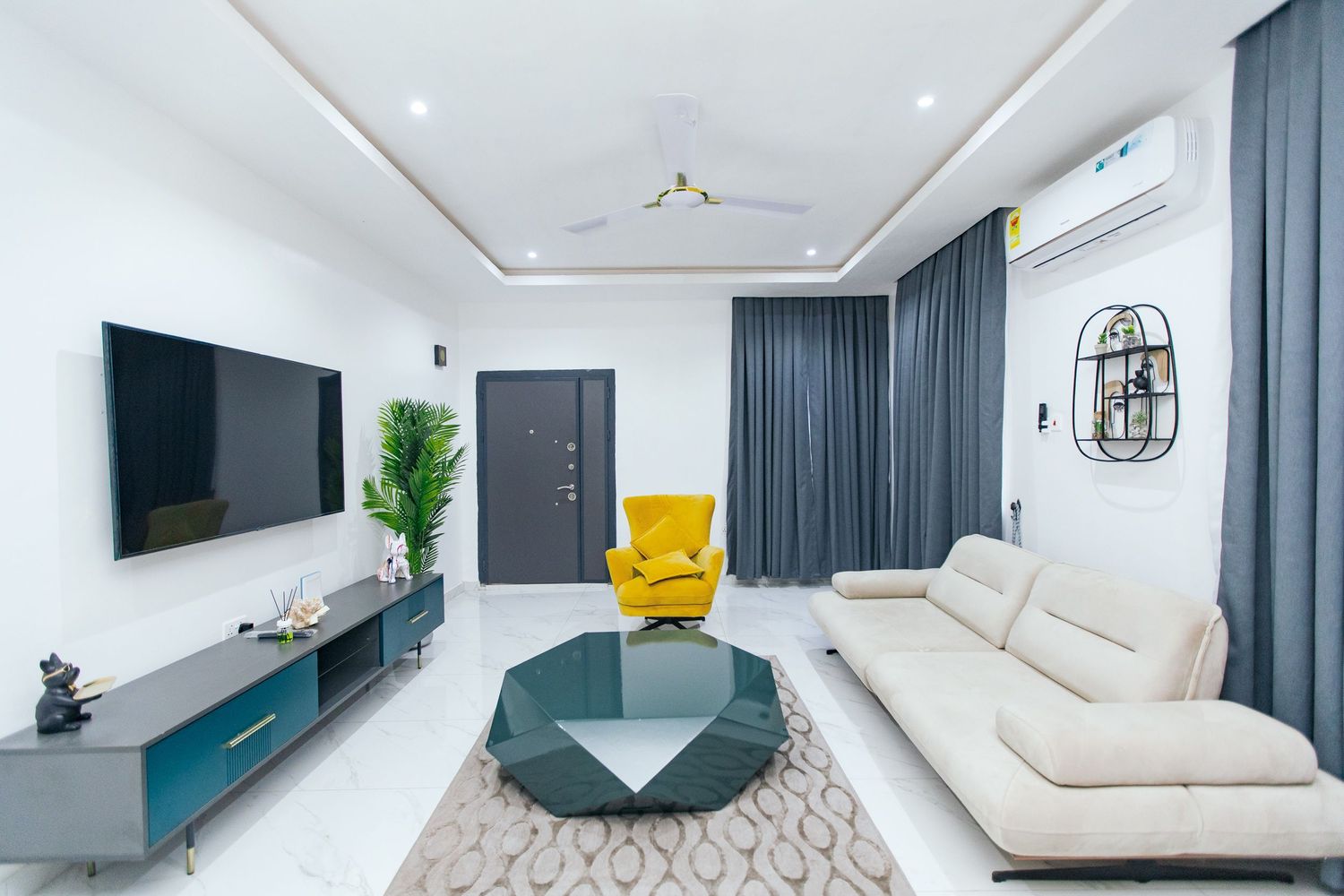 Minimalist living space with wall-mounted TV, grey curtains, and teal accent furniture against white walls.