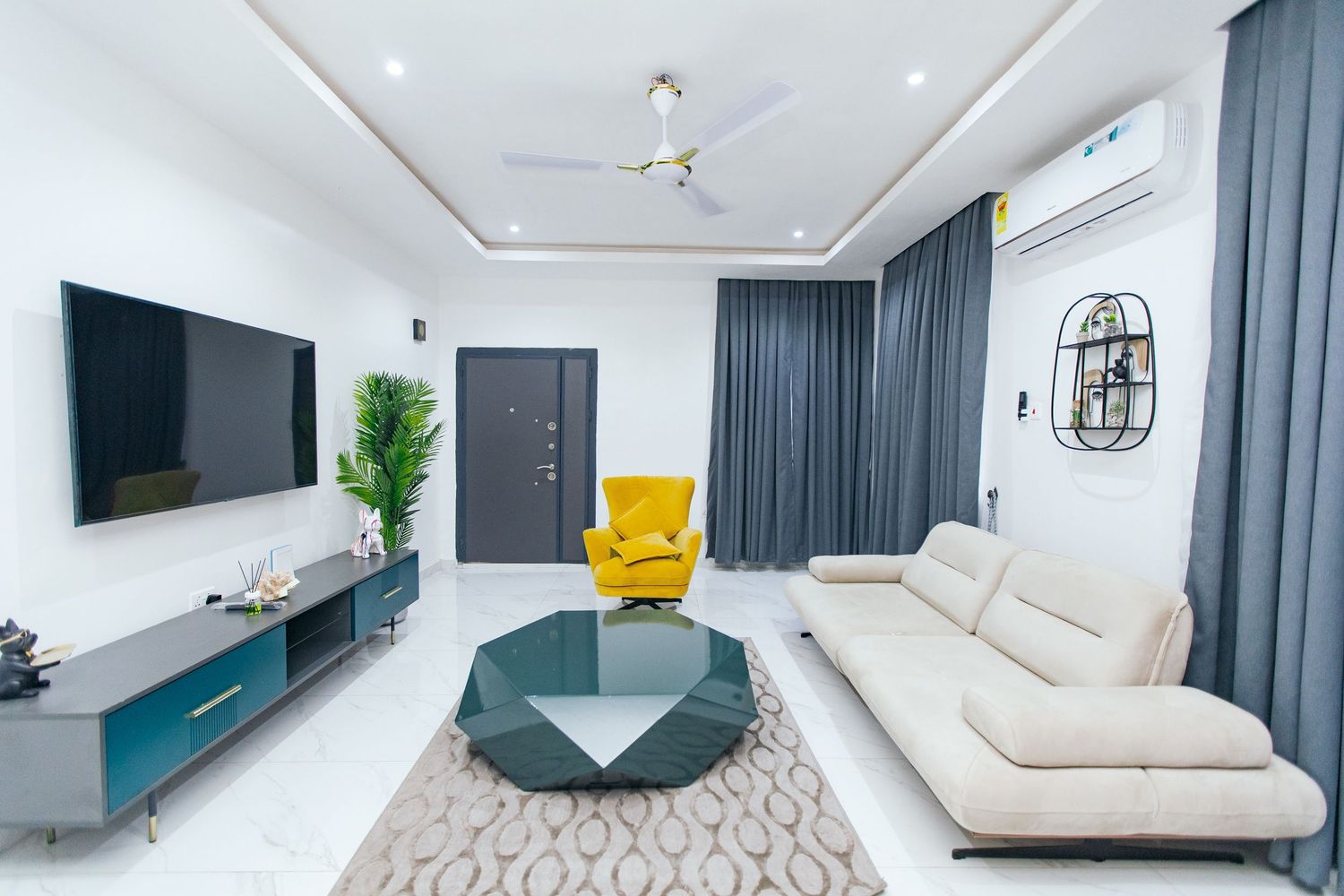 Contemporary open-plan living area with geometric patterns, teal sofa, and white ceiling lighting.
