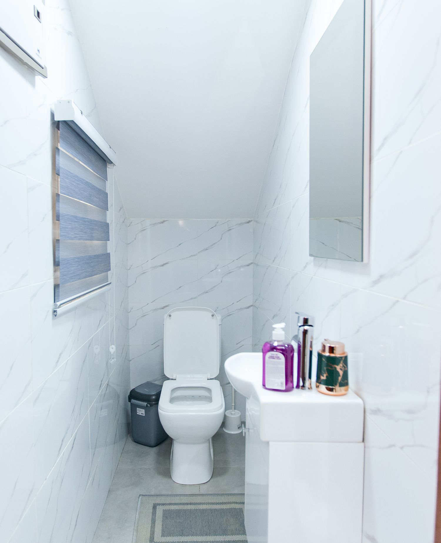 Modern white bathroom with marble-look walls, toilet, and toiletries on display.