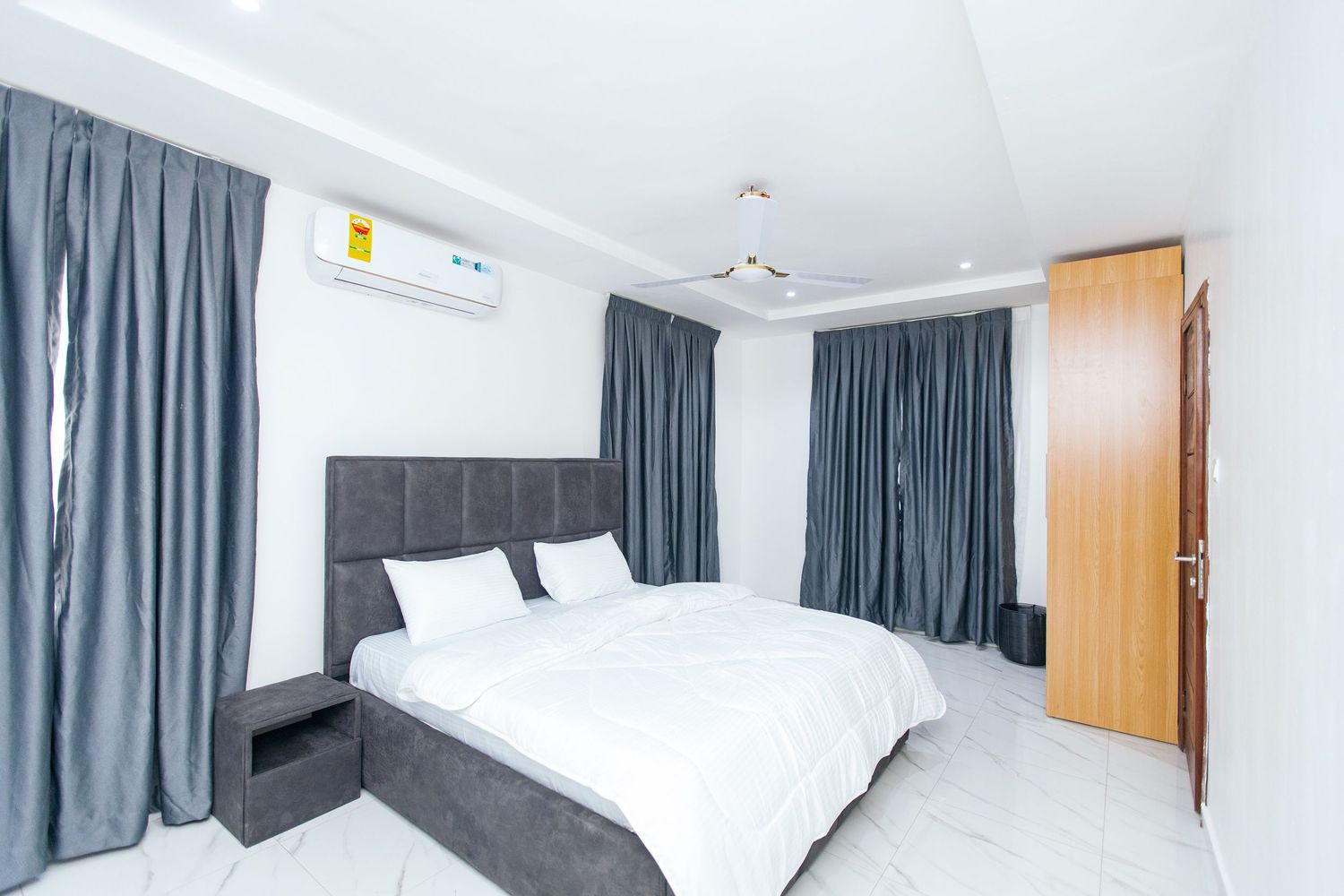 Spacious bedroom with white walls, dark curtains, and crisp white bedding.