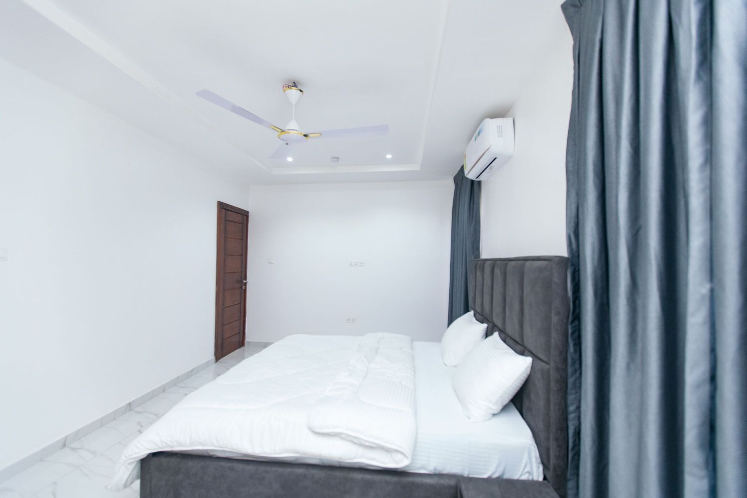 Contemporary bedroom design with dark curtains and white linens in natural light.