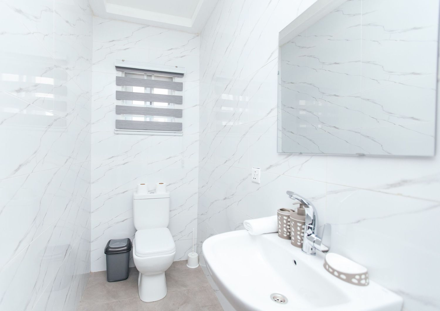 Sleek white bathroom featuring marble-style tiles and modern sanitary fixtures.
