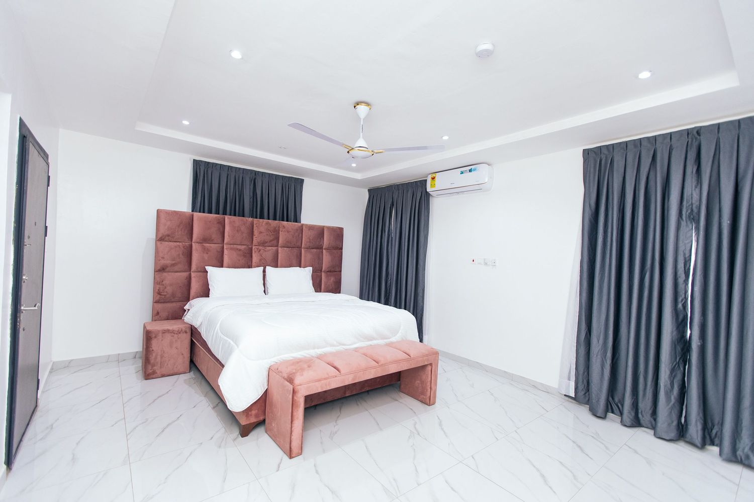 Modern bedroom interior with coral headboard and grey curtains against white walls.