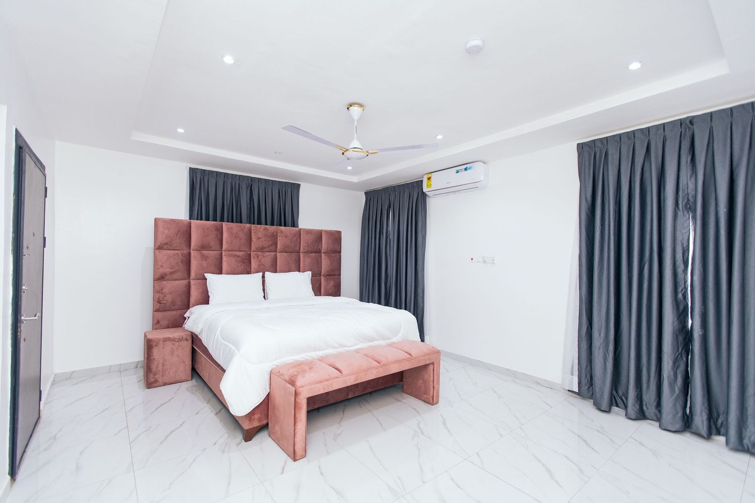 Modern bedroom interior with white walls, dark curtains, and a pink upholstered bed frame.