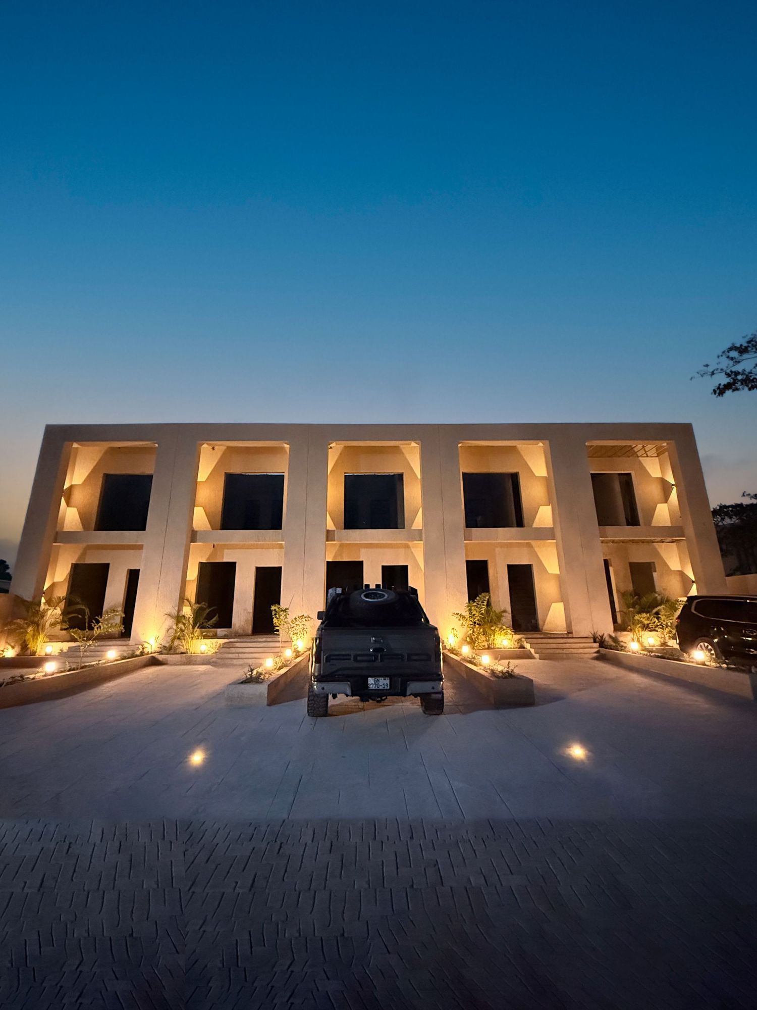 Modern white desert resort buildings illuminated at dusk with warm lighting against a deep blue sky.