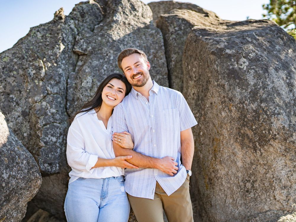 Couple in white and blue outfits share romantic moments against a rocky backdrop during an outdoor photo session.