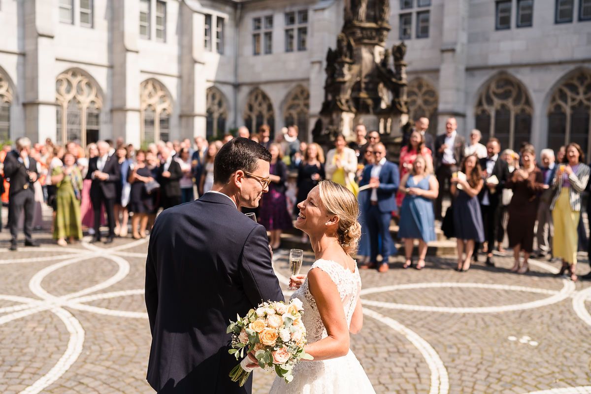Ein Brautpaar genießt einen romantischen Moment im Innenhof der Domsingschule, umgeben von Hochzeitsgästen.