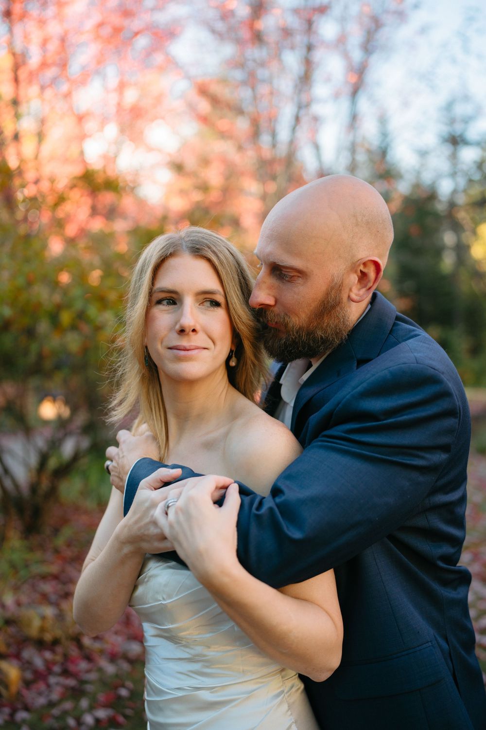 A romantic couple embraces outdoors during sunset while surrounded by autumn foliage.
