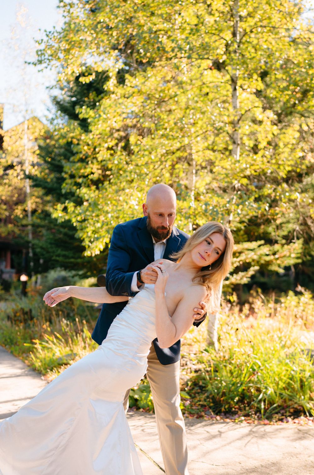 A couple dances playfully together in a golden autumn setting with sunlit trees in the background.