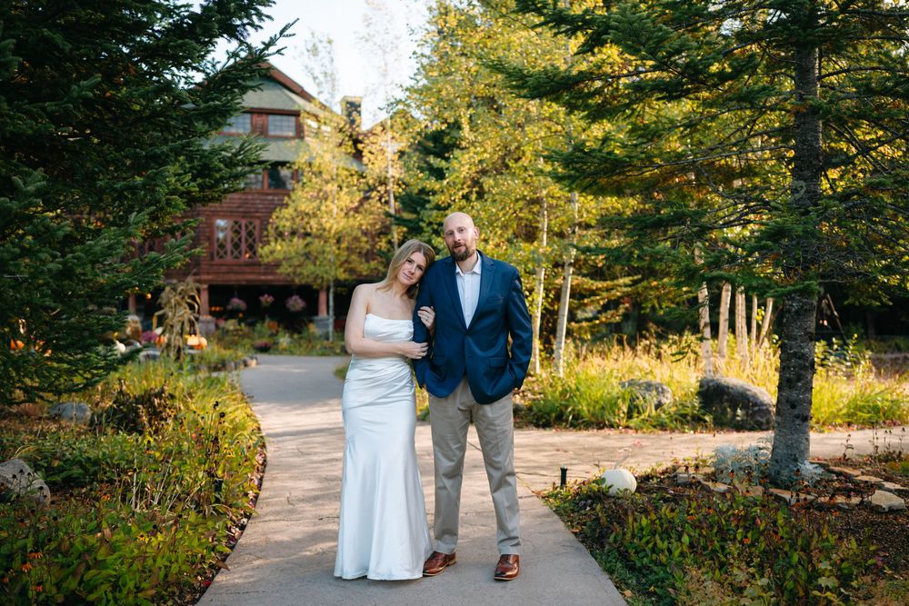 A couple walks together on a garden path surrounded by lush greenery and flowers in golden afternoon light.