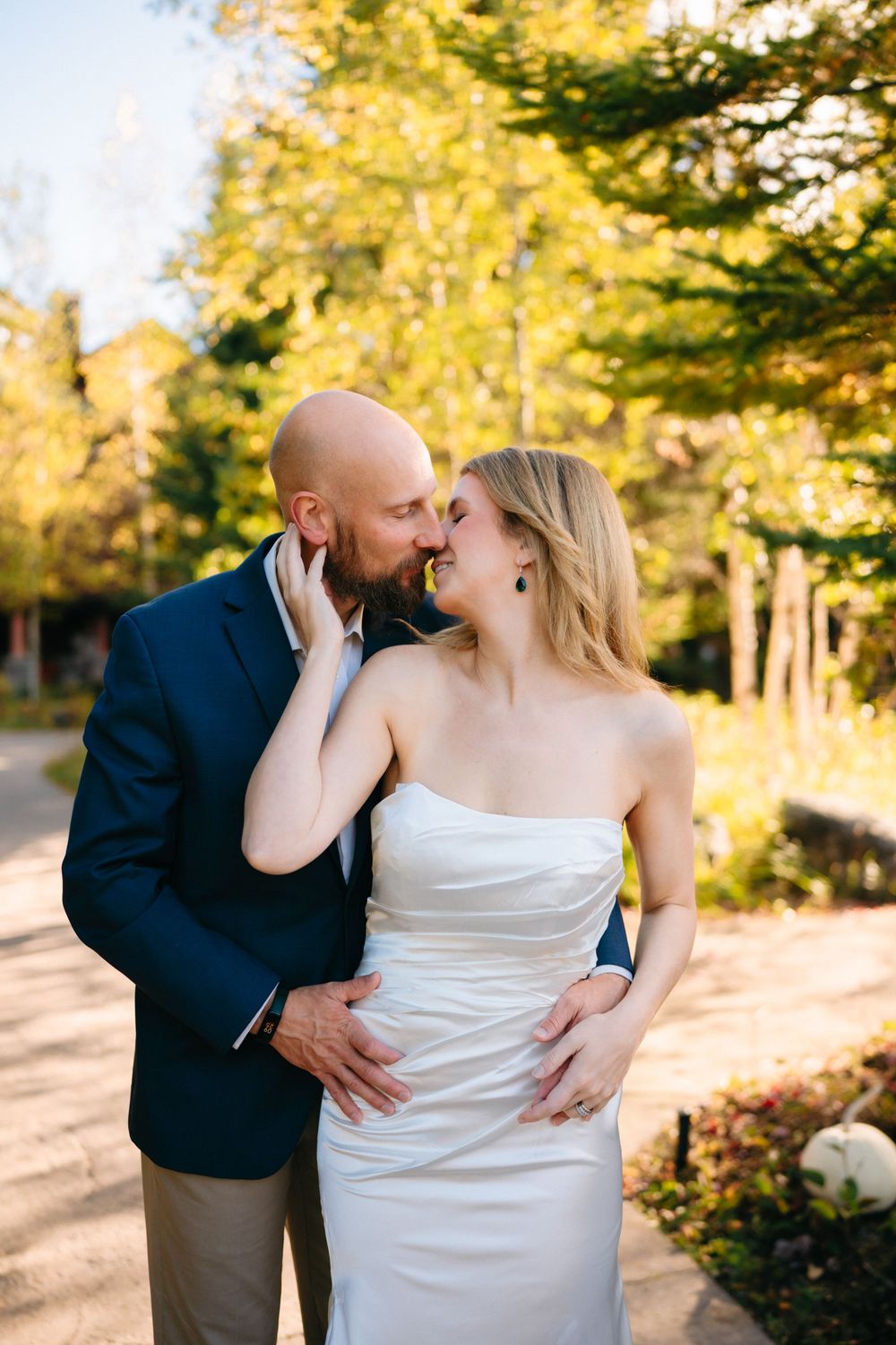 A romantic moment between newlyweds sharing an intimate embrace outdoors with autumn foliage in the background.