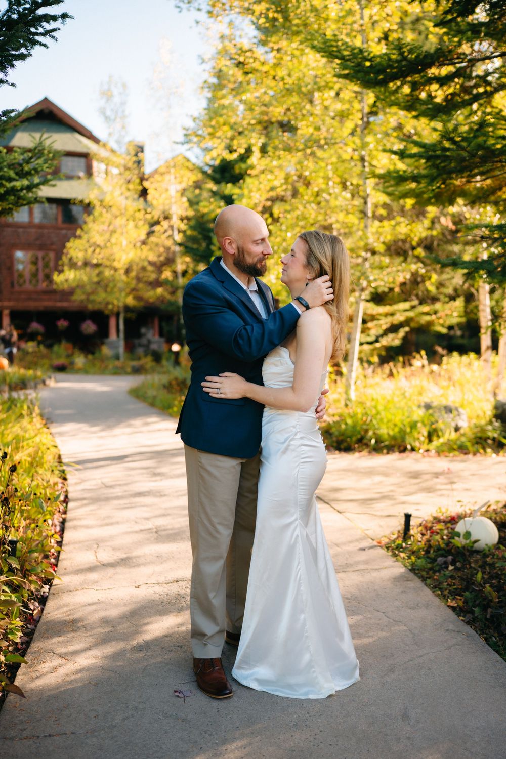 A couple shares a joyful moment together on a path surrounded by golden autumn trees and cabins.