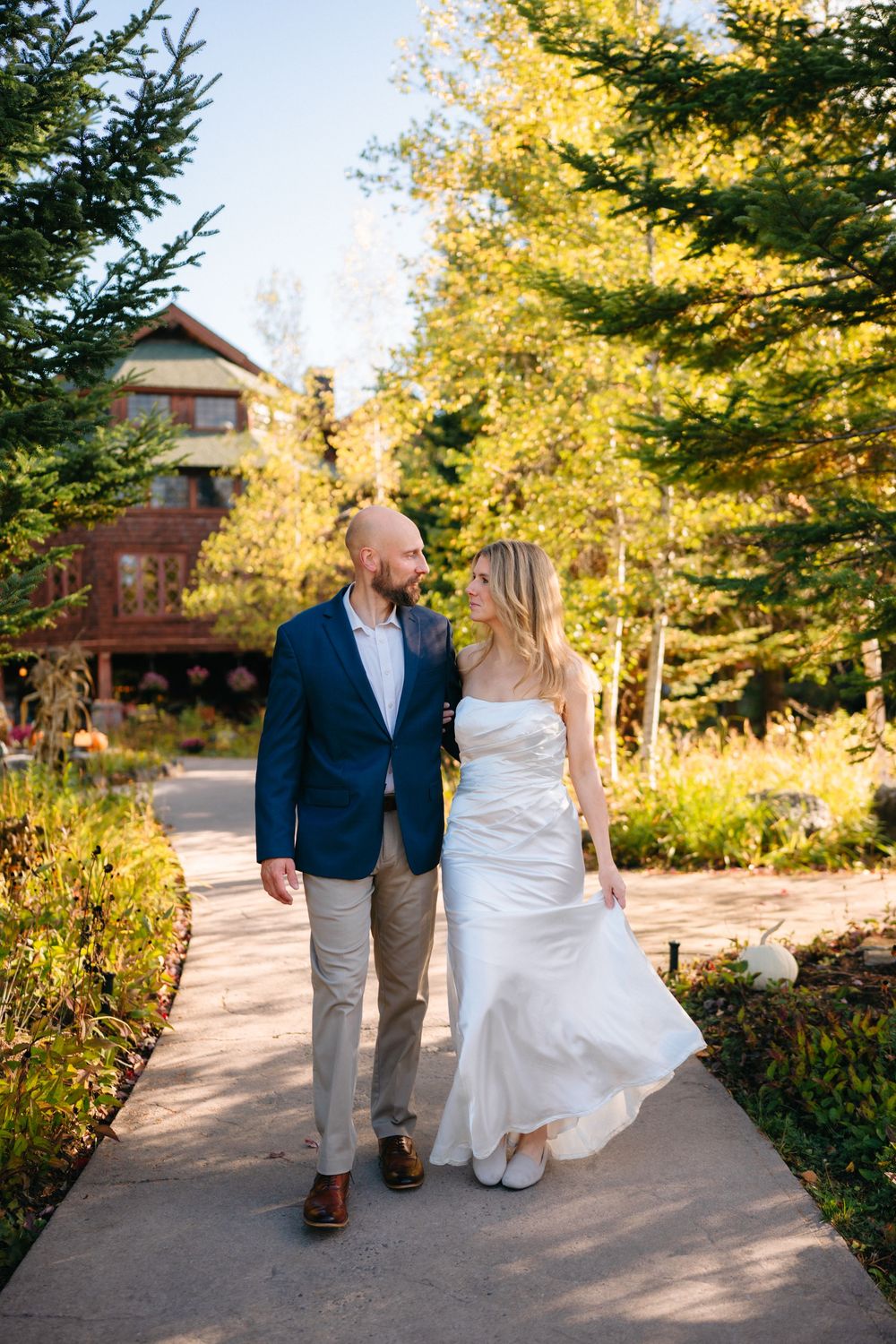 A couple walks together on a garden path surrounded by autumn trees and golden sunlight.