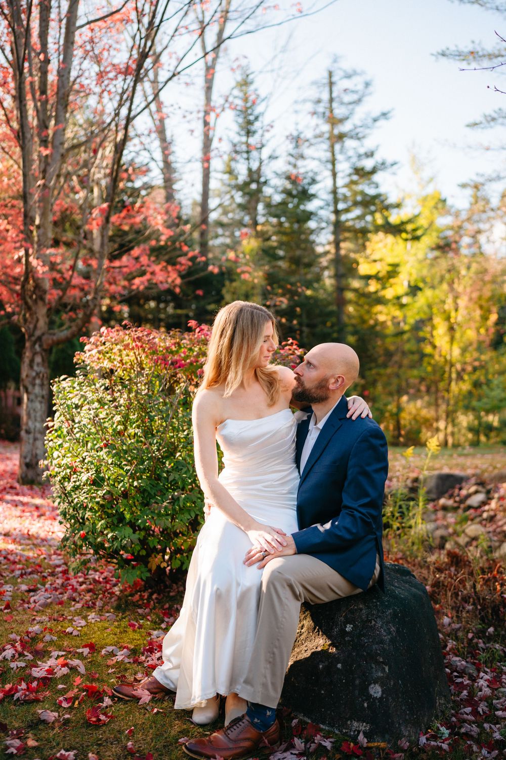 A romantic autumn engagement photoshoot among vibrant fall foliage and evergreen trees in a park setting.
