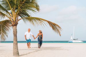 A romantic couple stands near palm trees on a pristine white sand beach with turquoise waters in the background.