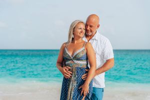 A couple embraces on a tropical beach with turquoise waters and white sand in the background.