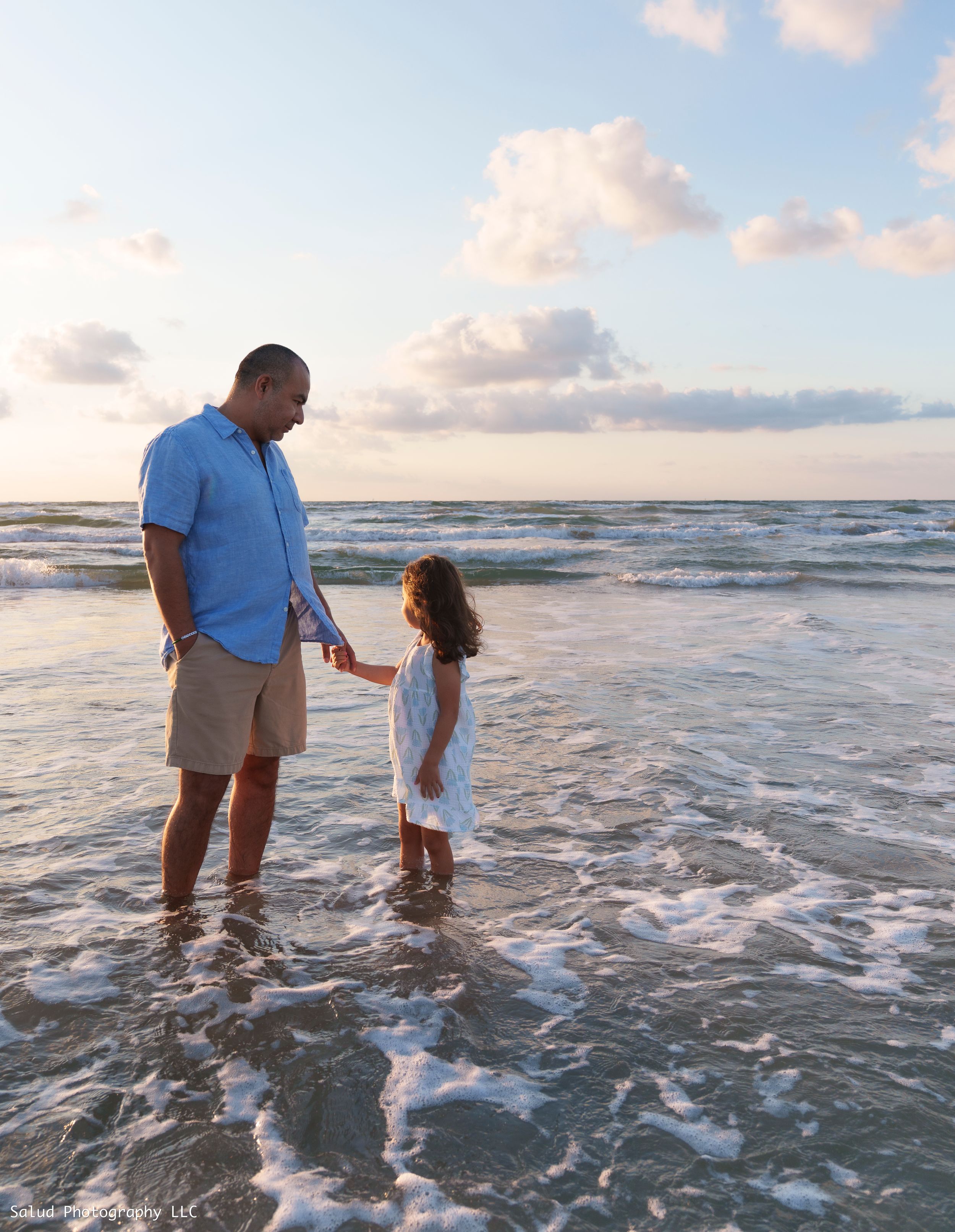 Father and child playing in ocean waves at sunset along the beach.