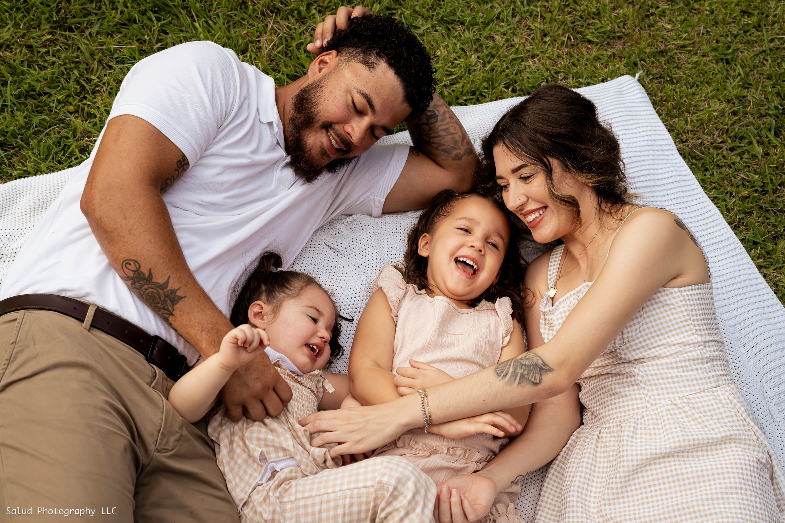 Family lying together on white blanket in grass during outdoor photo session.