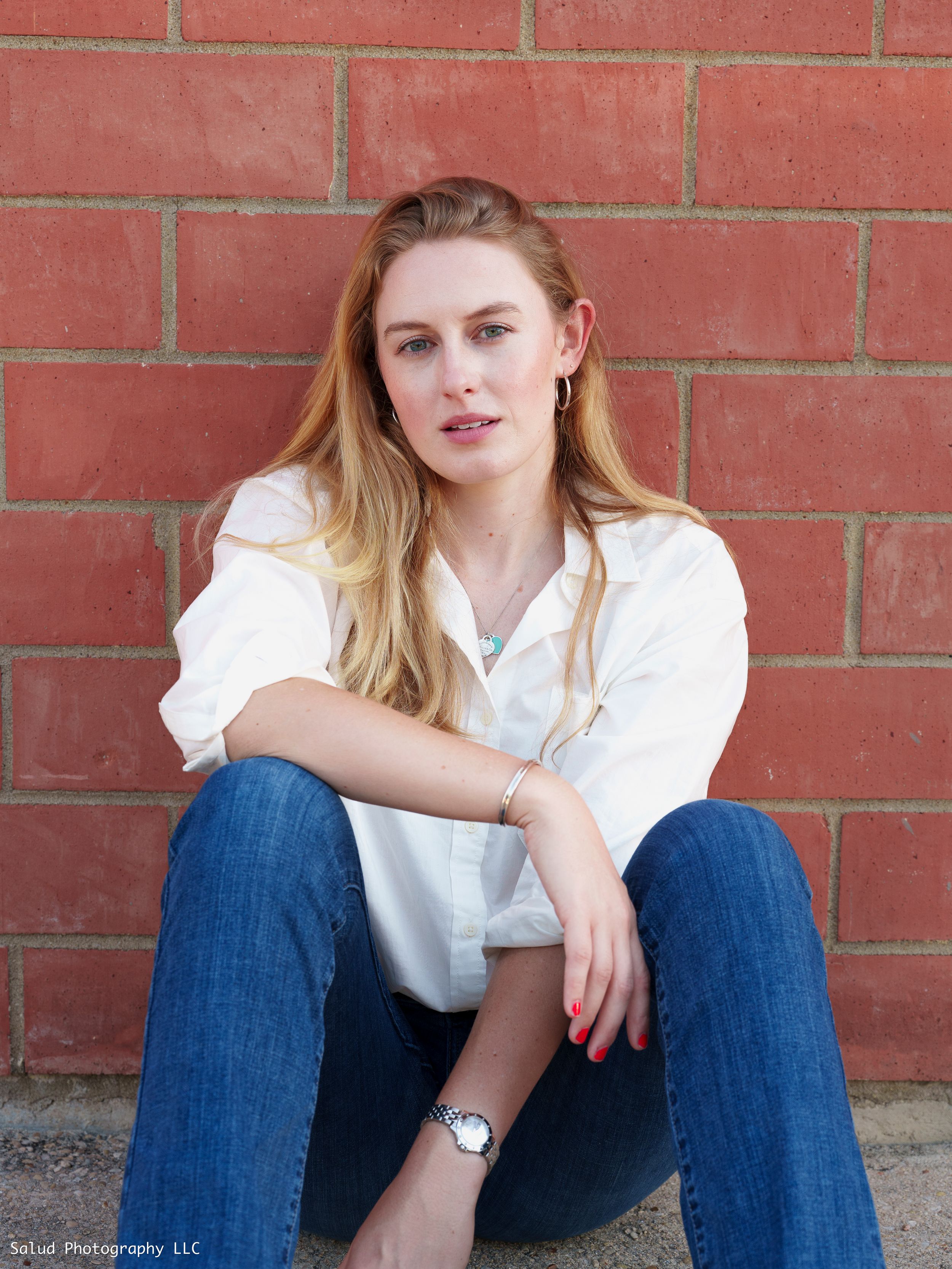 Casual portrait against red brick wall wearing white shirt and blue jeans.