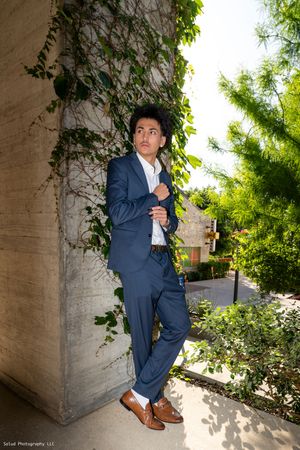 Stylish senior portrait series showing a student in a navy suit posing against a stone wall with greenery.