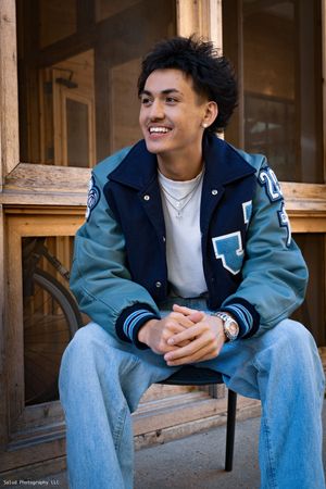 Casual senior portrait series of a student in a varsity jacket and jeans sitting on wooden steps.