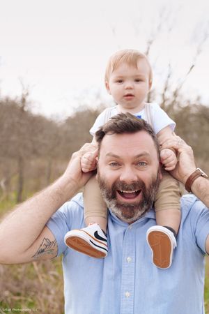 Playful series of a father giving his baby a shoulder ride outdoors in a light blue shirt.