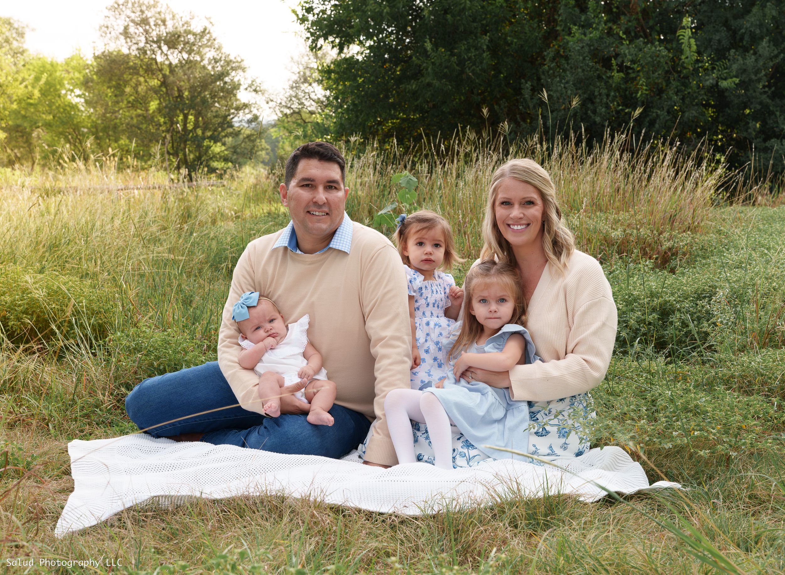 Family portrait session with parents and children relaxing on a blanket in a grassy field at sunset.