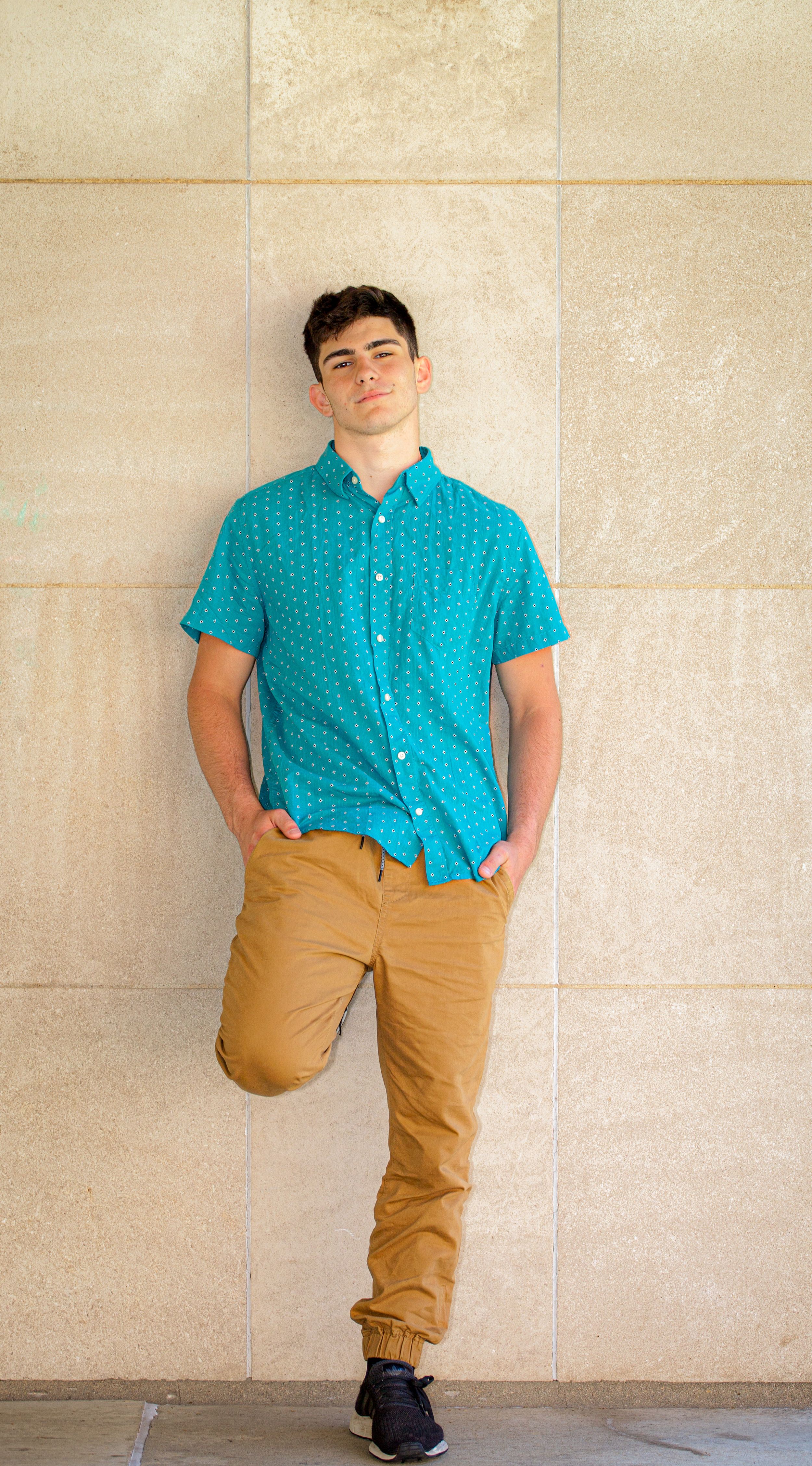 A series of casual fashion poses against a light wall wearing a turquoise patterned shirt and khaki pants.