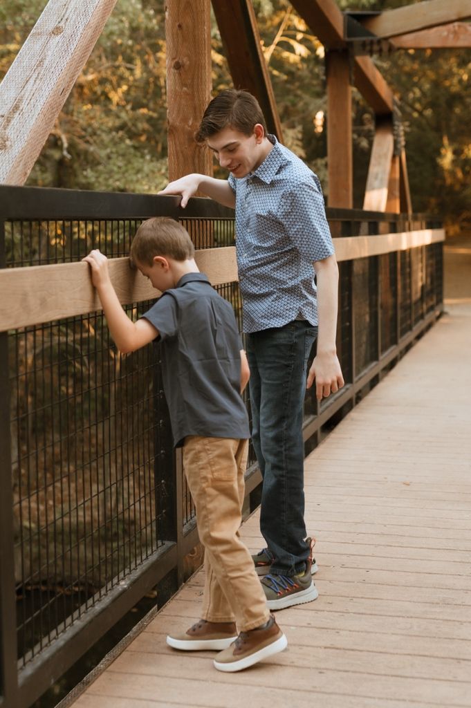 Two people playfully interact on a wooden boardwalk surrounded by autumn trees.