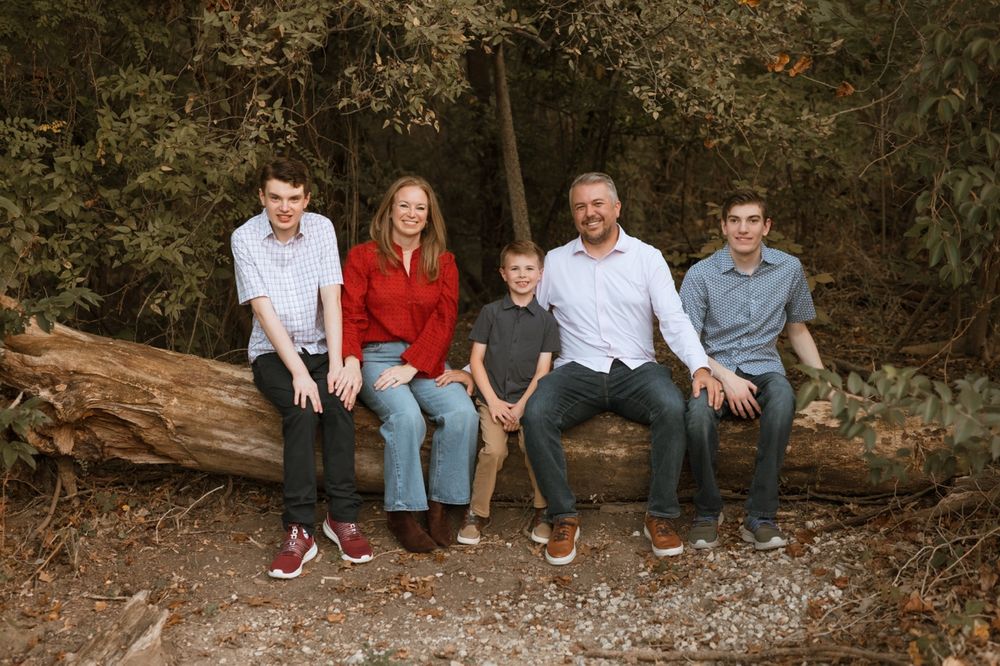A group sits together on a rocky ledge in a wooded outdoor setting during an autumn photoshoot.