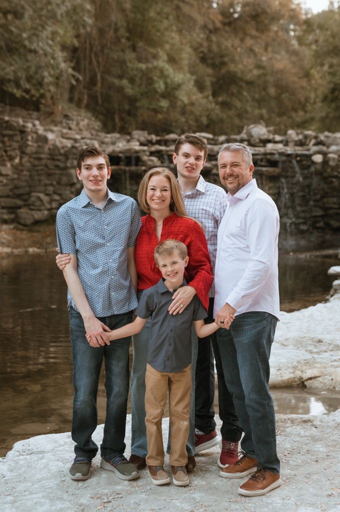 Family portrait session outdoors near a rocky waterfall with everyone dressed in casual coordinating outfits.
