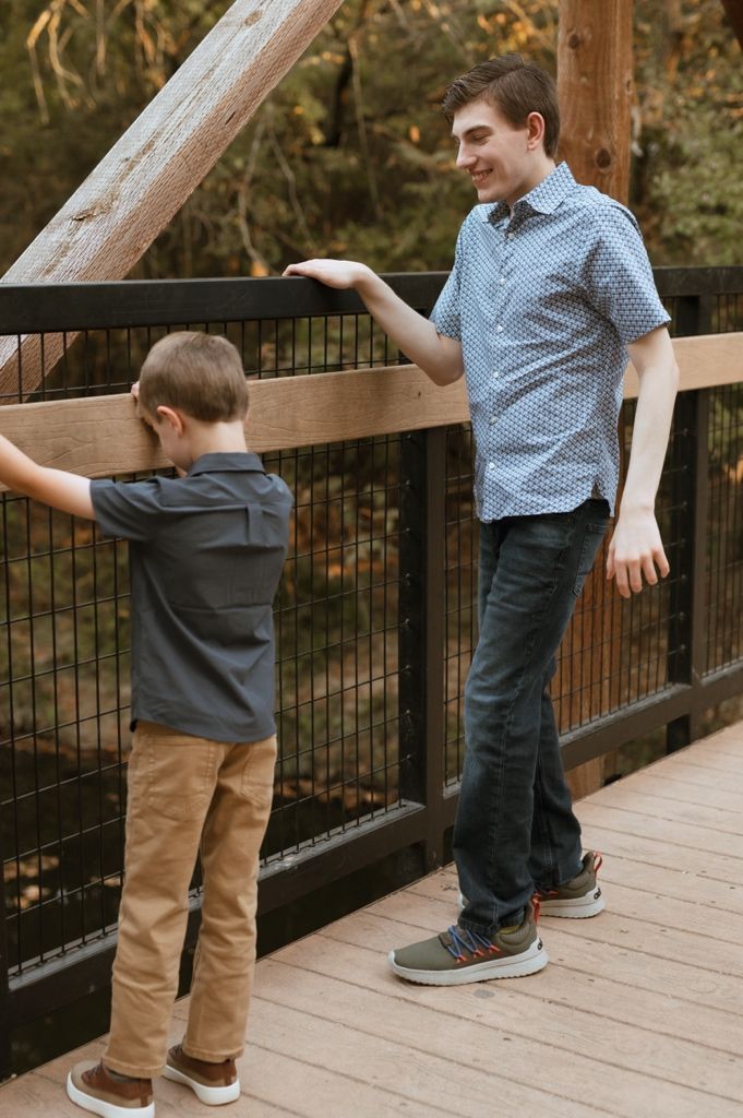 Two people in casual clothing interact playfully on a wooden deck surrounded by autumn foliage.