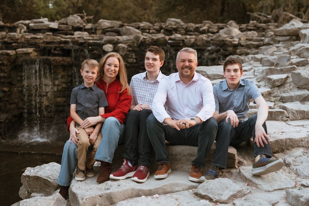 A group sits casually on rocky terrain near a waterfall during an outdoor photo session.