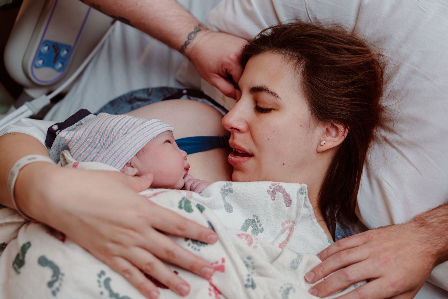 A mother and newborn baby share tender moments together while resting in a white hospital bed.