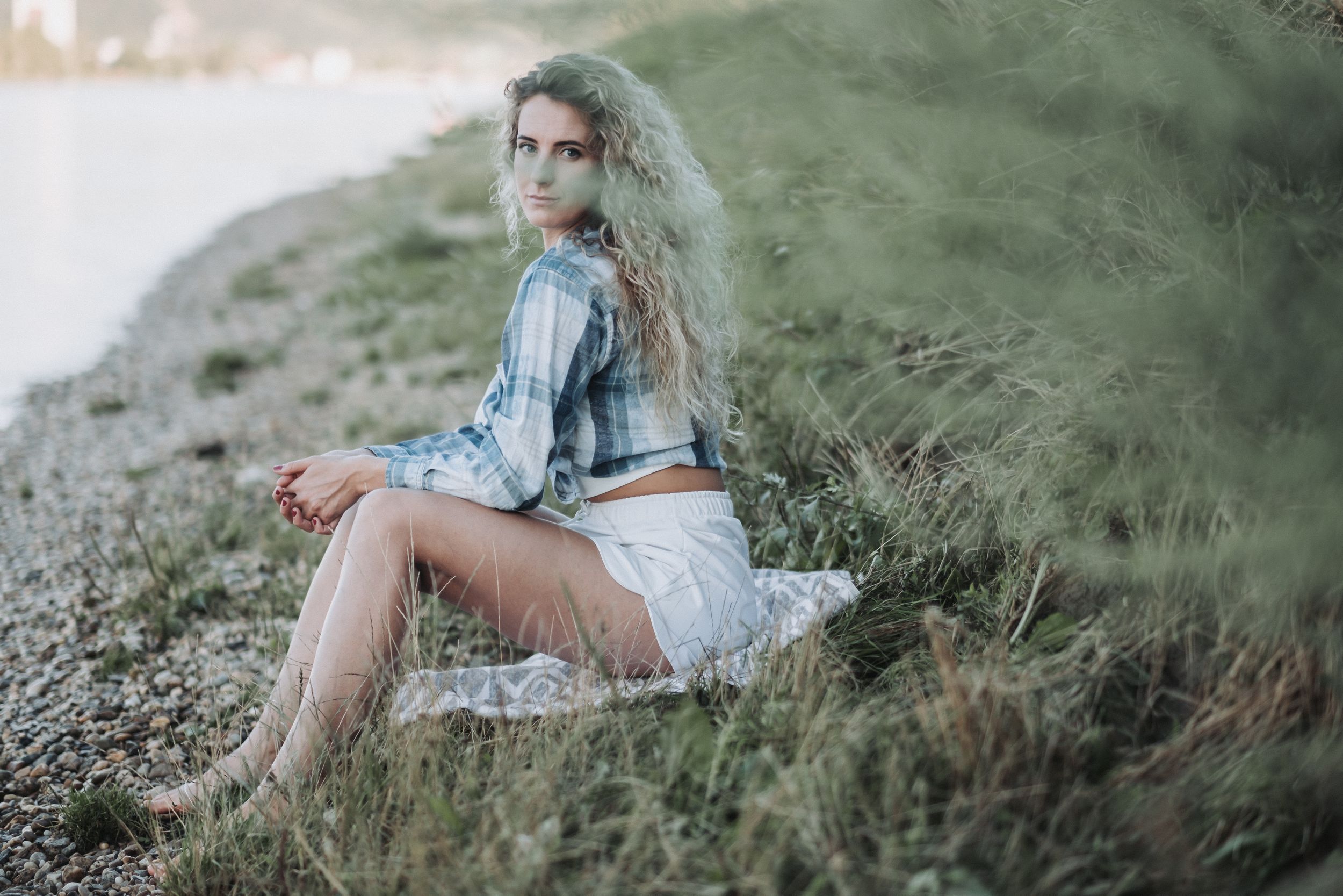 Someone in a denim jacket and white dress sits on a grassy hillside during a misty afternoon.