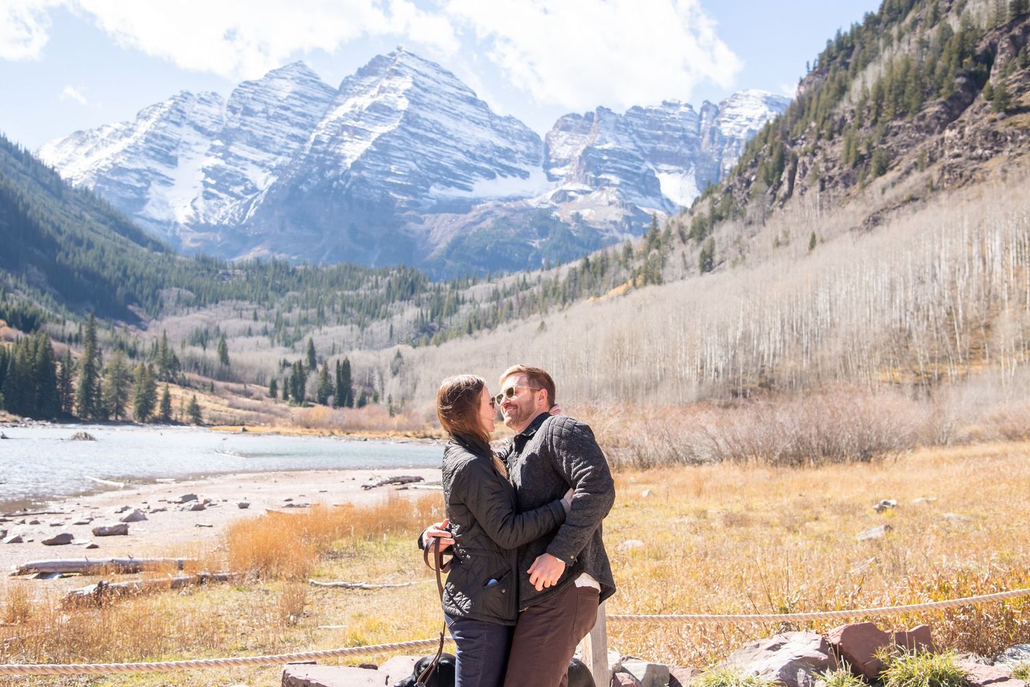 Couple embraces in front of snow-capped Maroon Bells mountains during autumn in Aspen, Colorado.