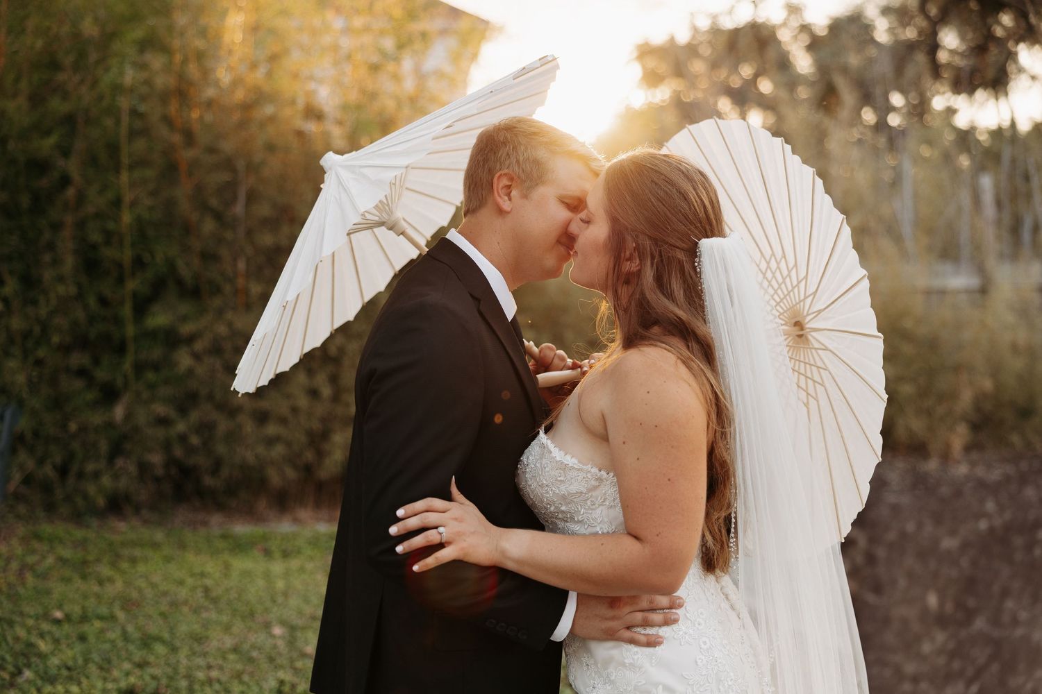 Newlyweds embrace in romantic dip pose with flowing wedding dress at outdoor venue.