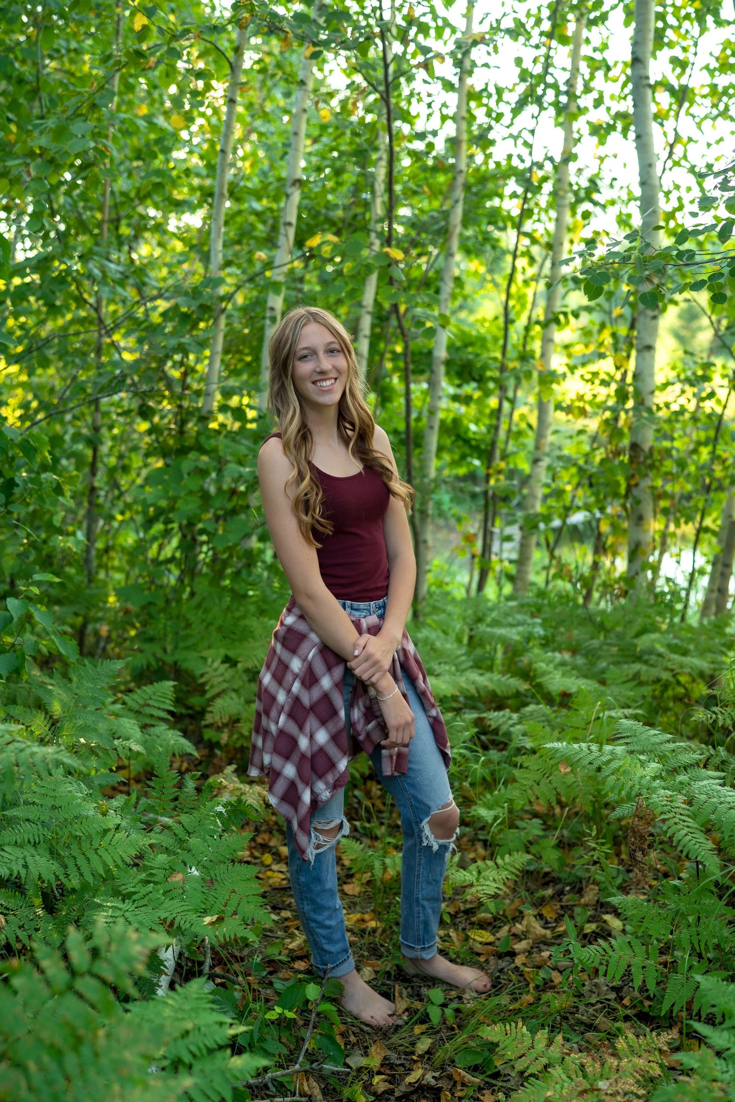 A casual outdoor photoshoot in a lush forest setting with ferns and dappled sunlight.
