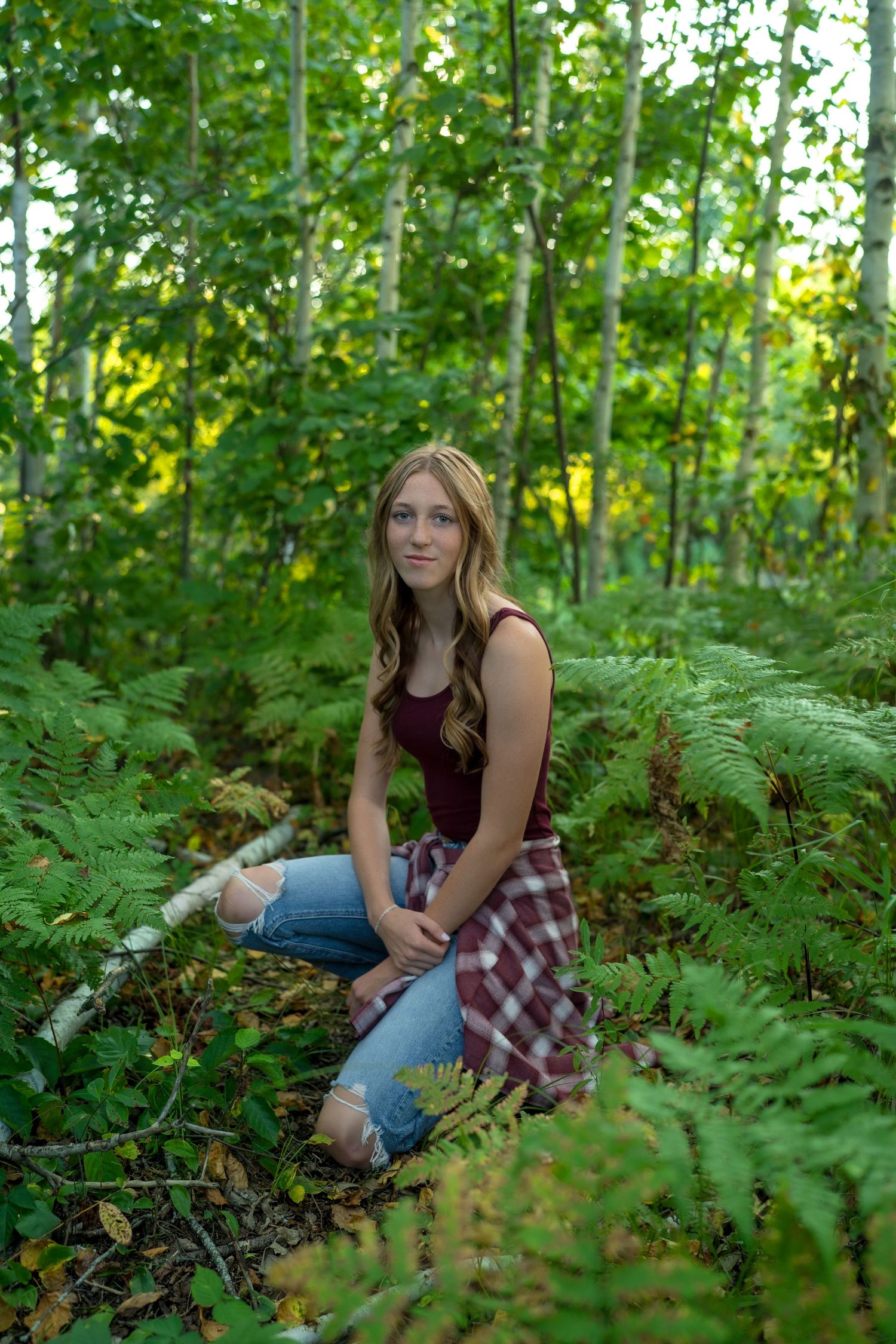 Person lying in lush green ferns and forest undergrowth wearing plaid shirt and jeans in natural outdoor setting.