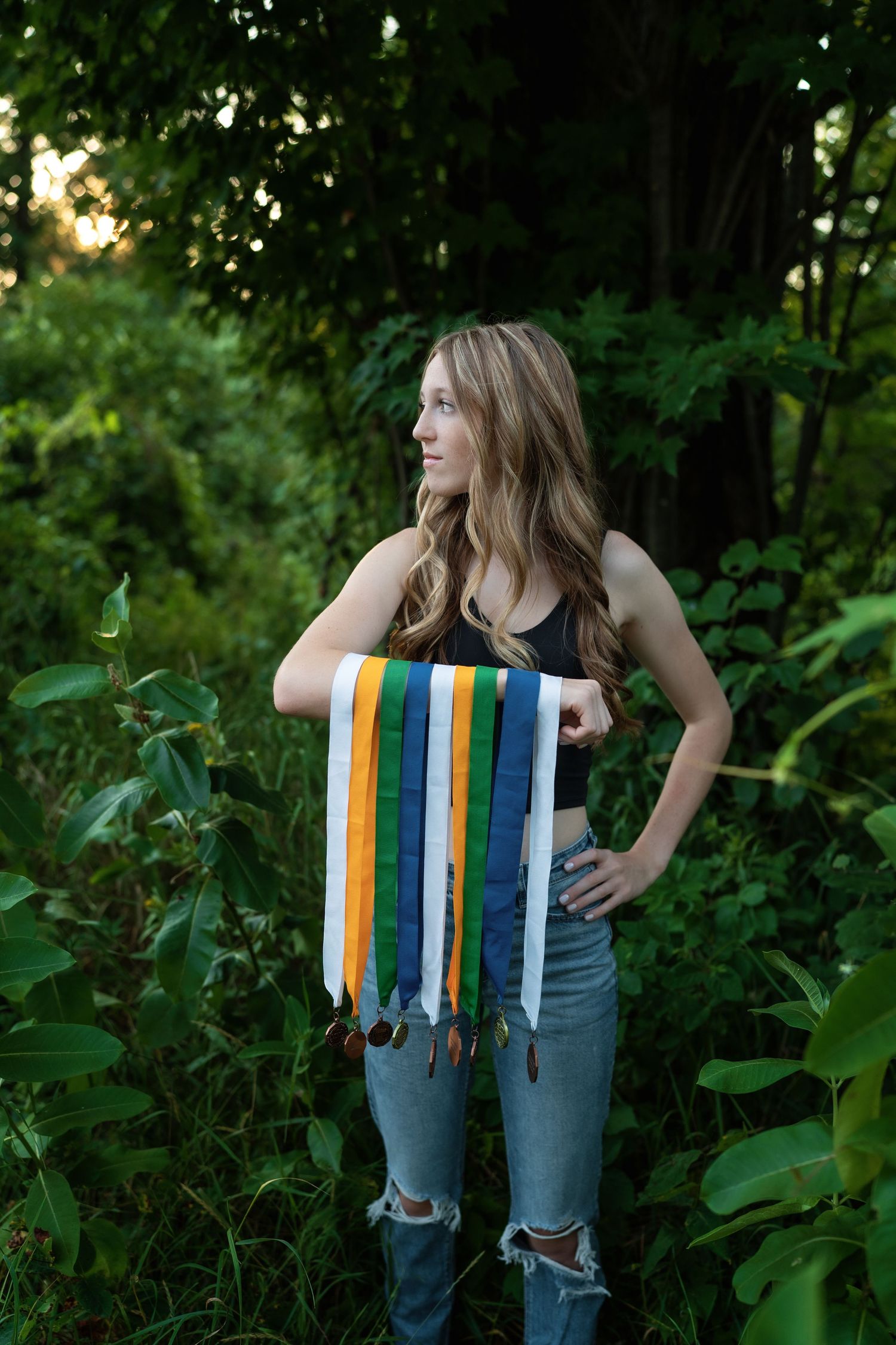 Artistic portrait session against green foliage wearing distressed jeans and colorful striped accessories.